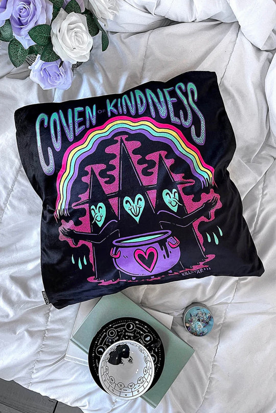 A black pillow cushion with rainbow colors featuring a witch, purple pot and Coven of Kindness text in aqua and purple.
