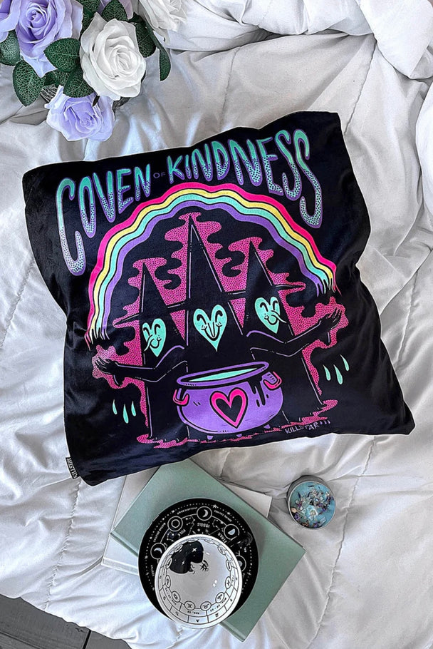 A black pillow cushion with rainbow colors featuring a witch, purple pot and Coven of Kindness text in aqua and purple.
