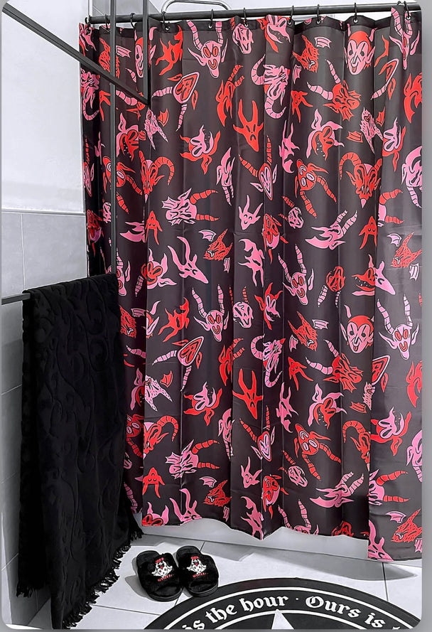 A black shower curtain with red and pink characters on it hanging on a shower rod in a bathroom.