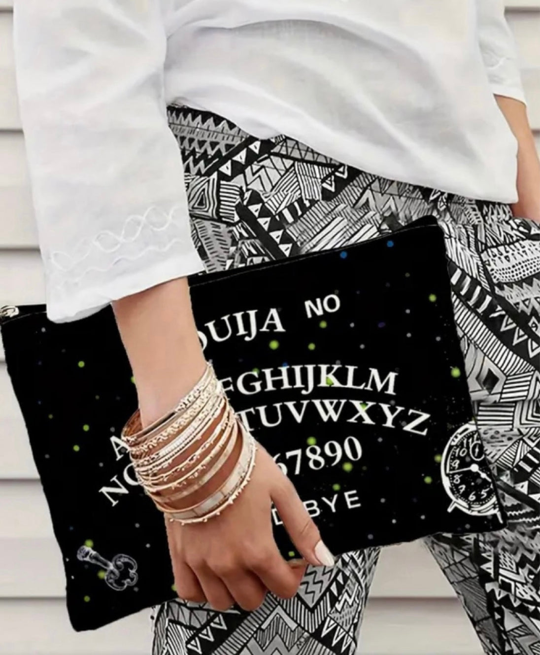 A woman carrying a gothic print makeup bag in black with “ouija yes no goodbye “ written on it.