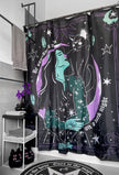 A black shower curtain with white text, a woman, cat, moon and stars hanging on a shower rack in a bathroom.
