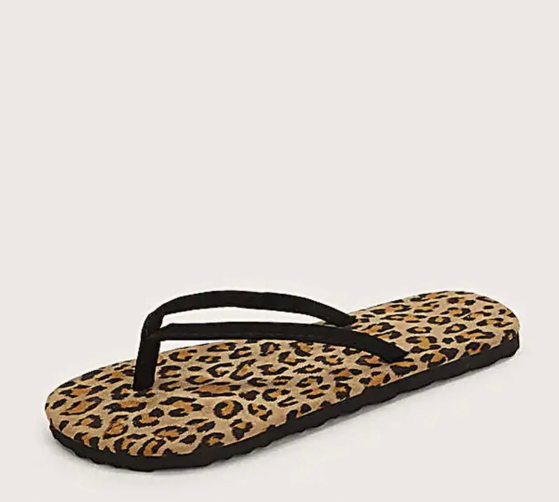 A close up of one leopard patterned flip-flop showcased on a tan background.