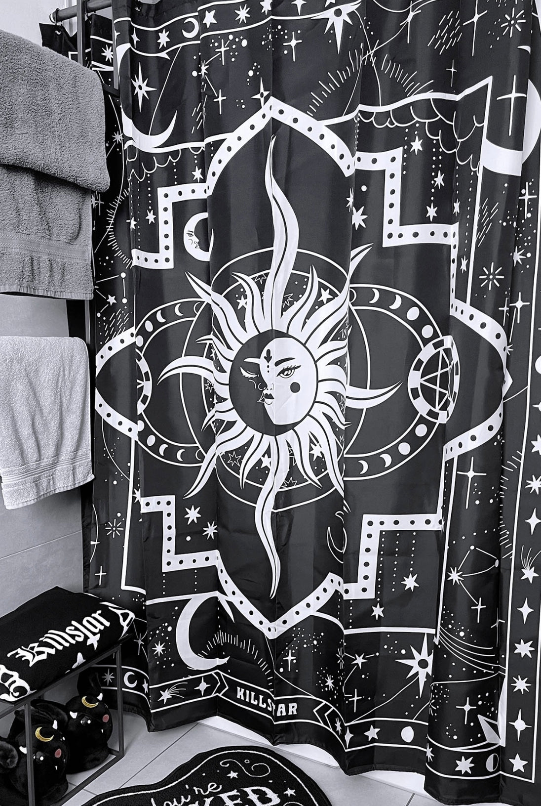 A black and white shower curtain with a white sun hanging on a shower rod in a bathroom.