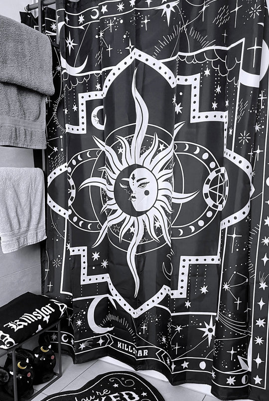 A black and white shower curtain with a white sun hanging on a shower rod in a bathroom.