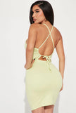 The back view of a female wearing a lime green mini dress with a cut out and crisscross back.