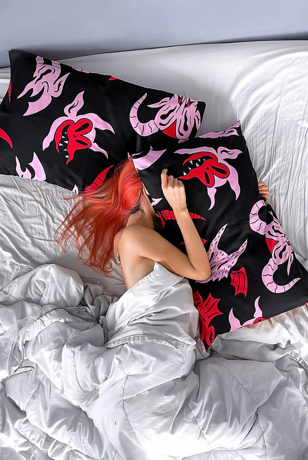 A woman laying jn bed with two black pillows with pink and red characters.